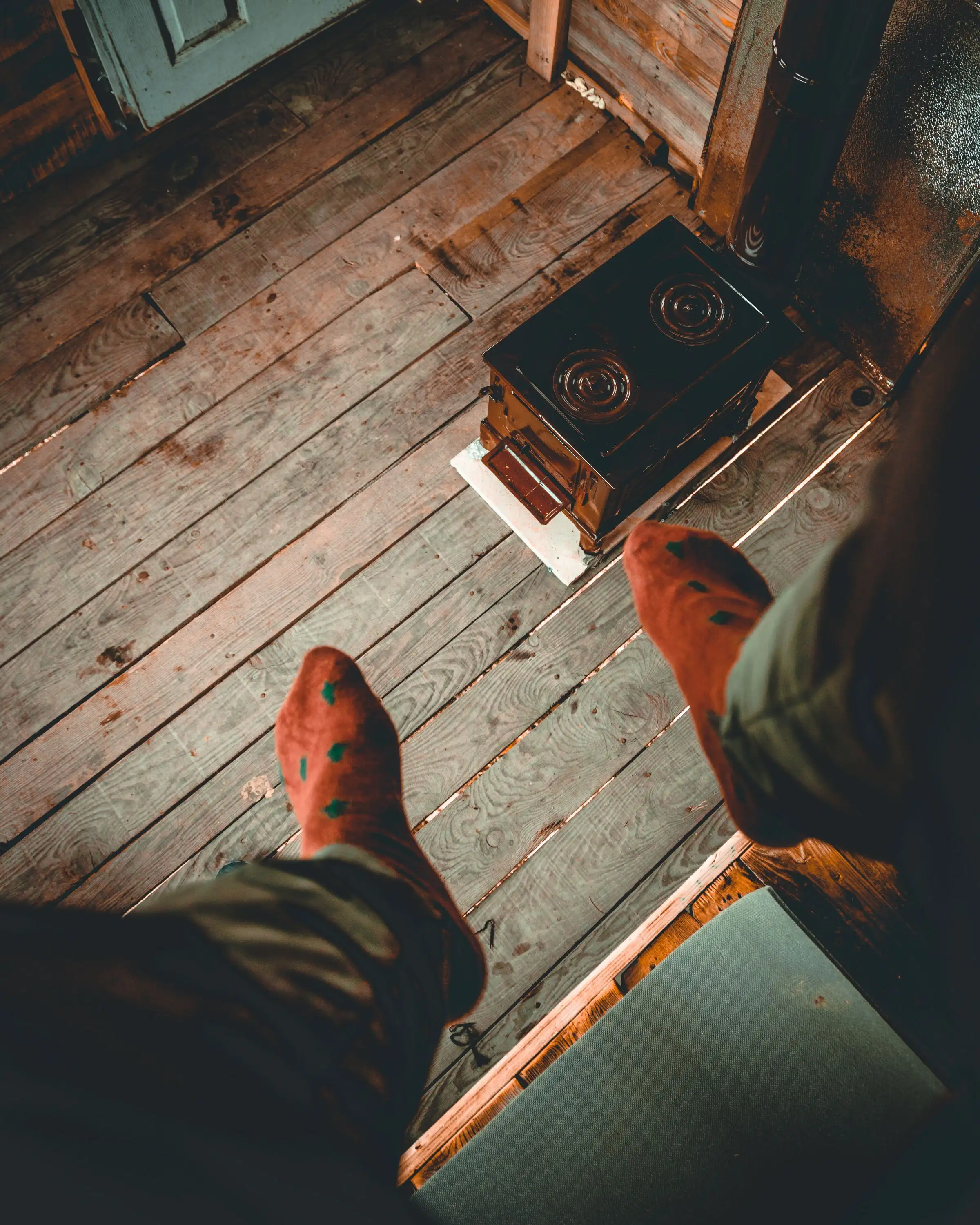 Pies con calcetines junto a una estufa de leña, sobre piso de madera