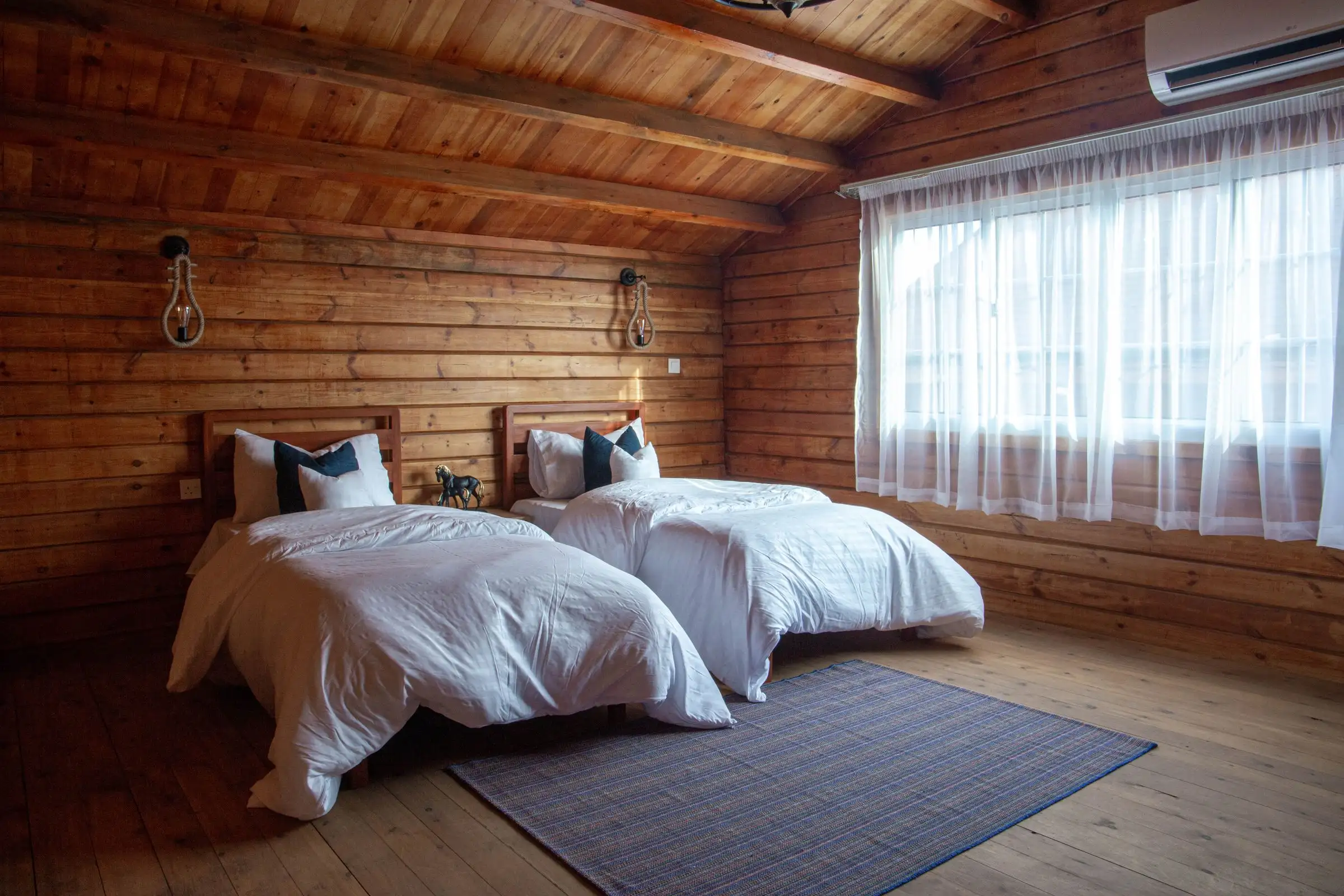 Recámara de madera con dos camas y cortina clara