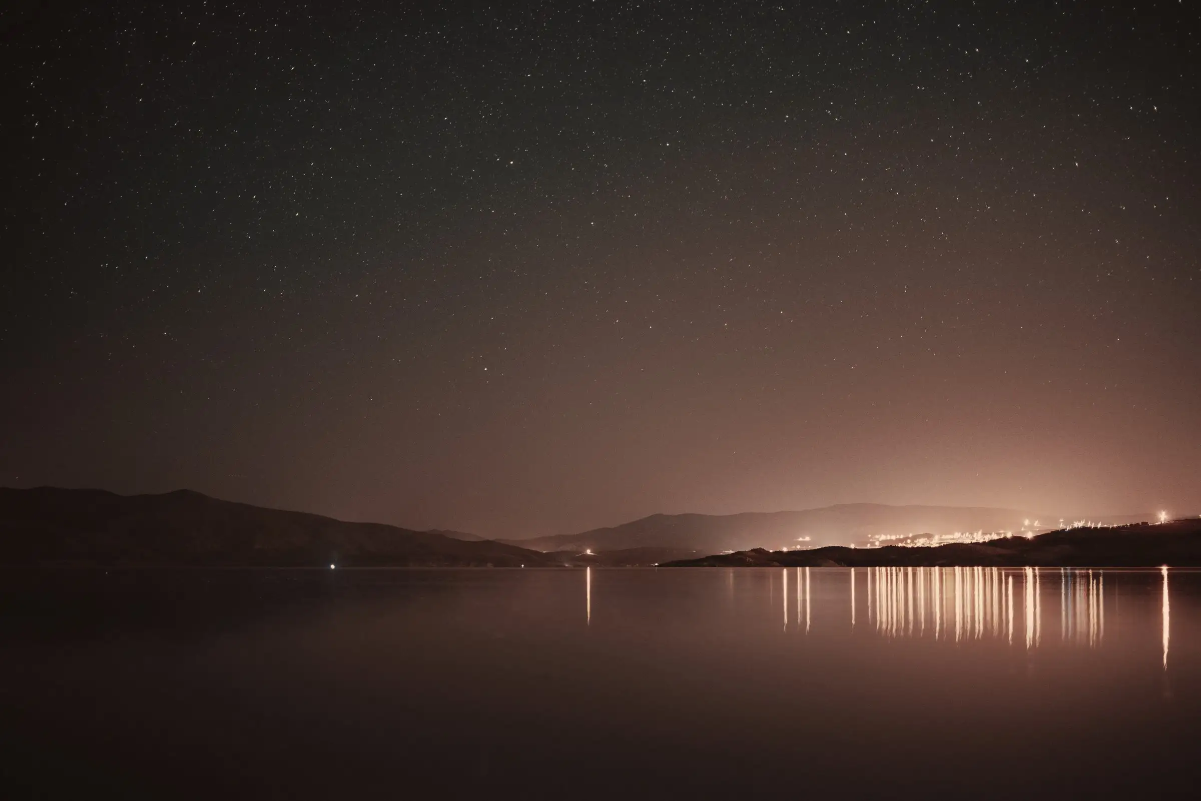 El lago de noche, con las luces de un pueblo reflejadas en el agua y cerros al fondo